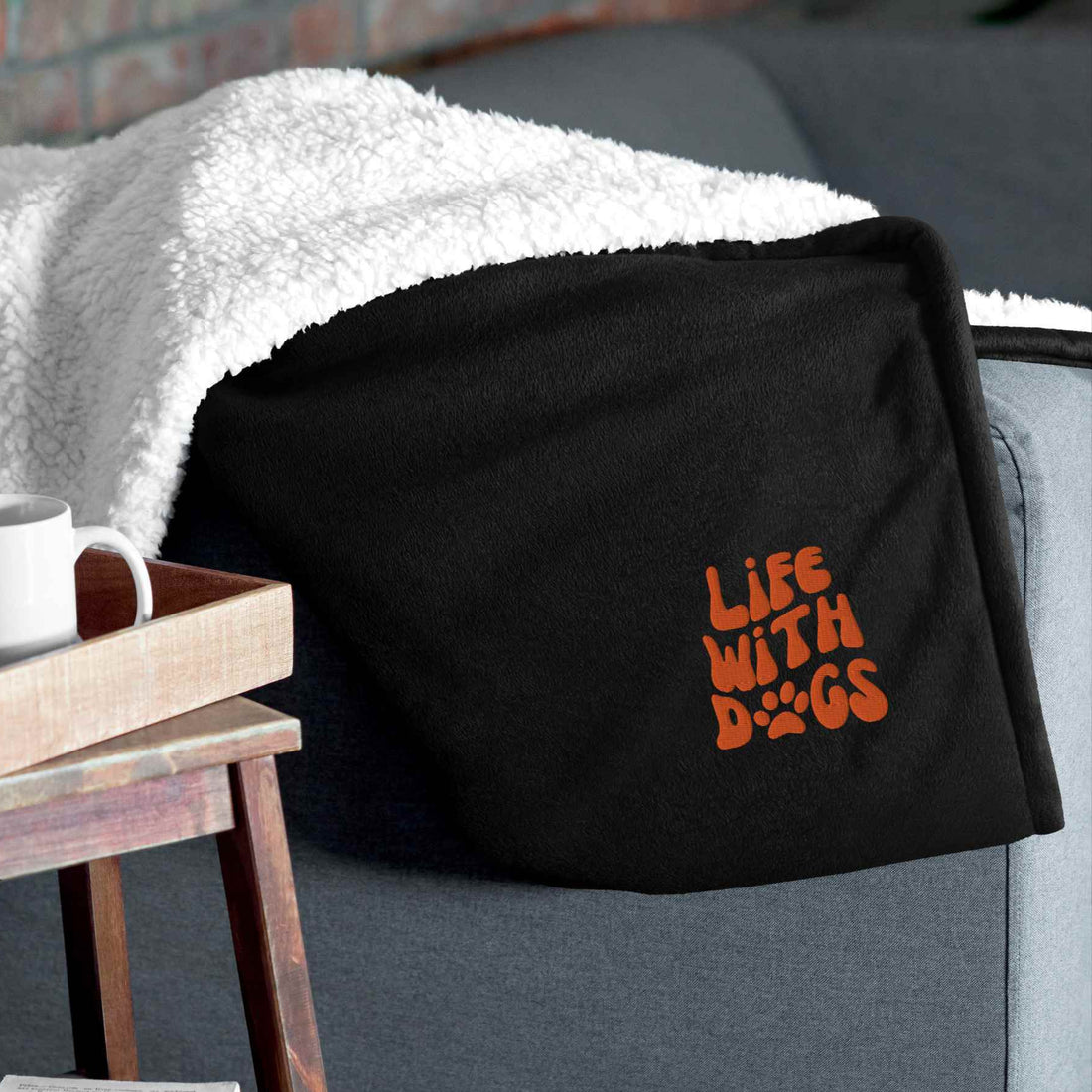 Black sherpa blanket with LIFE WITH DOGS embroidery on corner displayed on couch edge showing premium quality