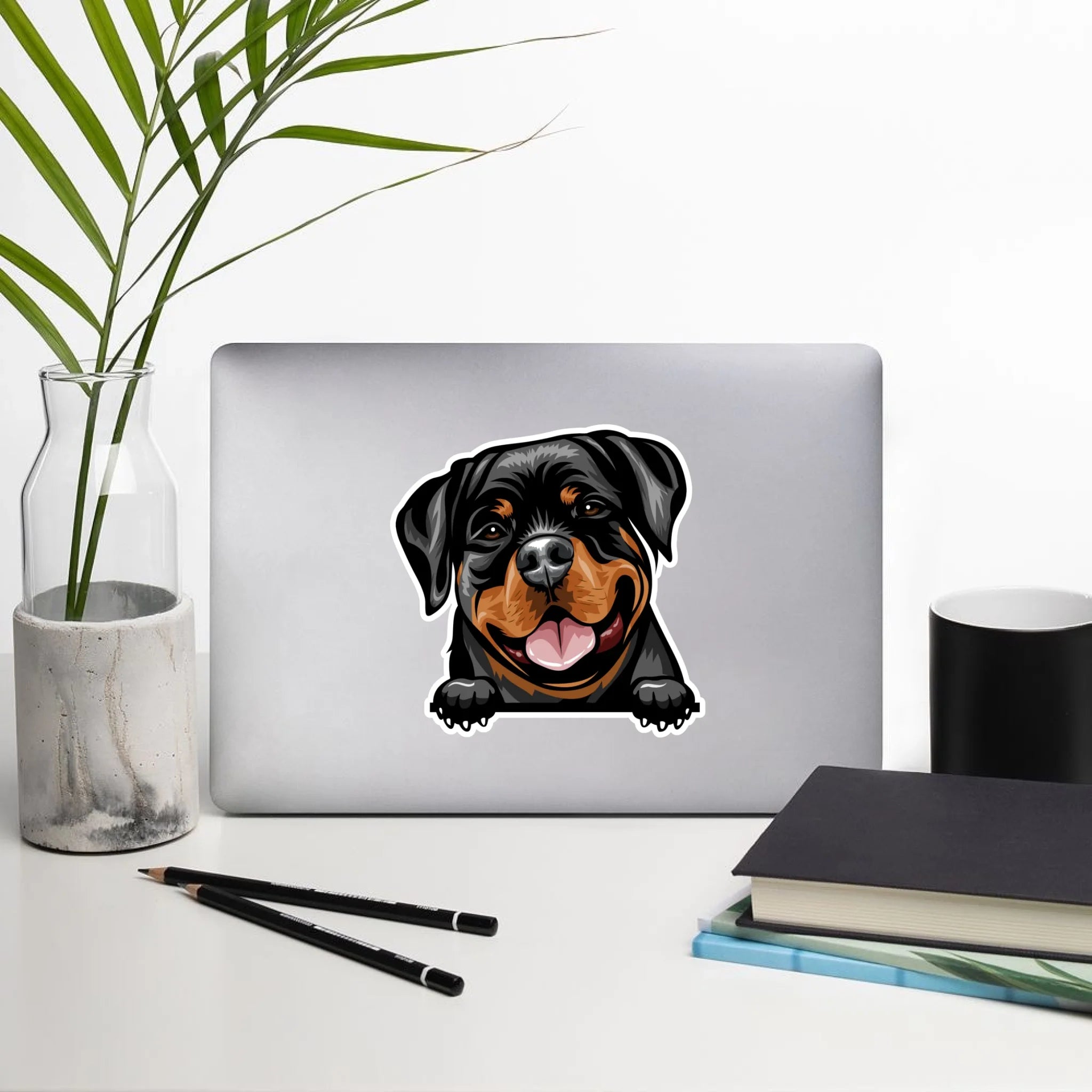 Laptop with a Rottweiler sticker on a desk with a plant, pencils, and notebook.