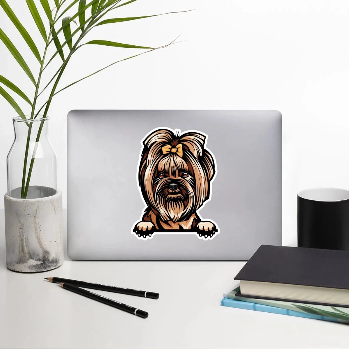 Yorkshire Terrier sticker on laptop on a desk with a plant, mug, and books
